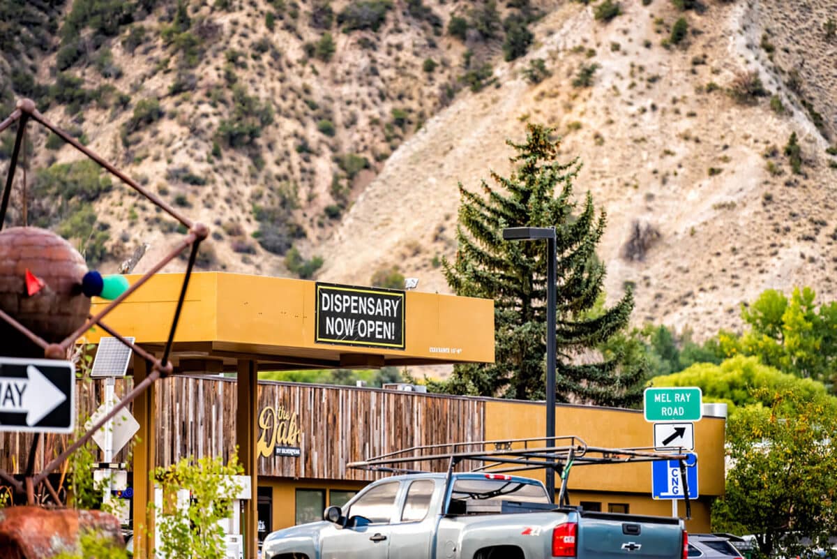 Recreational cannabis dispensary on downtown city street of Colorado with open for business sign to represent a blog about buying weed while out of state.