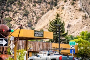 Recreational cannabis dispensary on downtown city street of Colorado with open for business sign to represent a blog about buying weed while out of state.